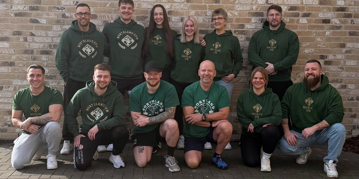 Das Team des Northland Gym in grünen Vereins-Hoodies vor der Backsteinwand des Studios